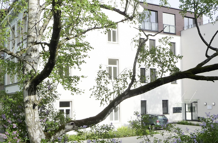 Das Bild zeigt das Praxis Gebäude von Außen, ein weißes Haus umwachsen von Bäumen.